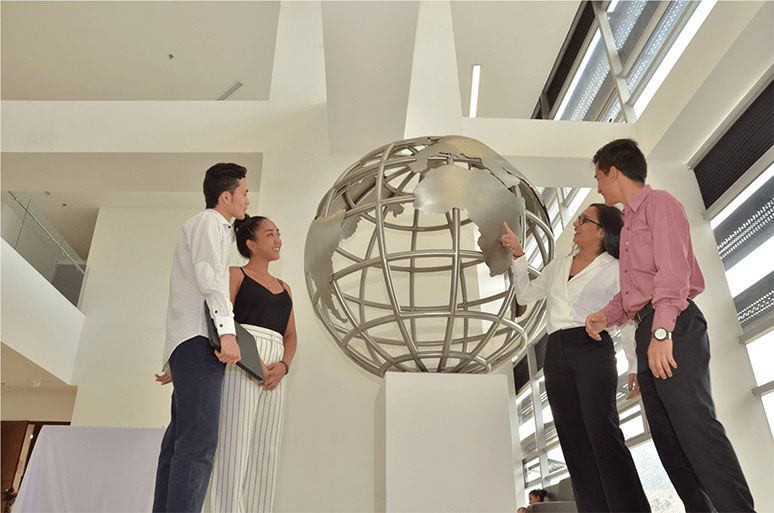 Imagen de personas alrededor de una escultura en acero que representa el globo terráqueo, imagen de cabecera para la Facultad de Ciencias Económicas Unibagué